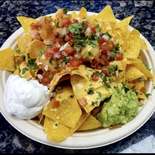 A plate of Beach Tacos nachos with cheese, salsa, guacamole, and sour cream.