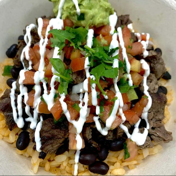 Mexican rice bowl with steak, black beans, pico de gallo, sour cream, and guacamole.