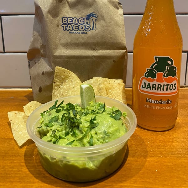 Guacamole with lime and cilantro, tortilla chips, a Beach Tacos bag, and a Jarritos soda.