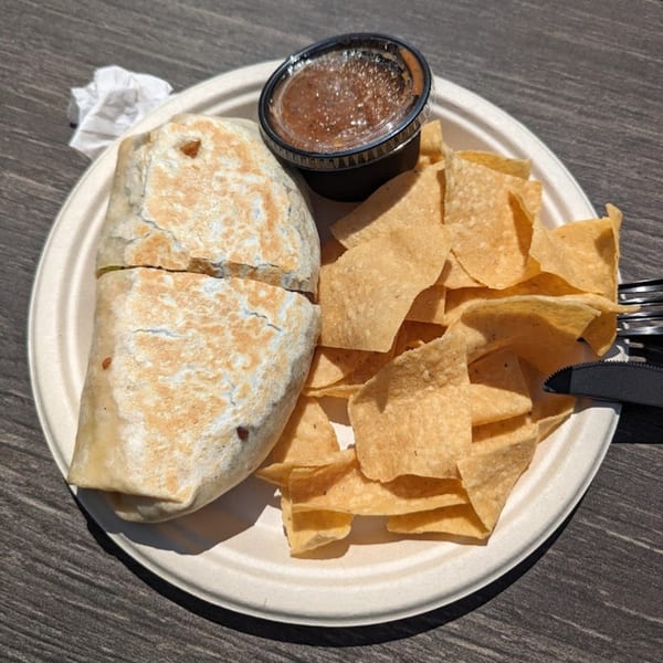 A Beach Tacos burrito, tortilla chips, and salsa on a white plate.