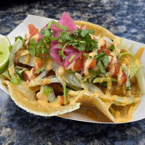 A Beach Tacos fish taco with lettuce, pico de gallo, pickled onions, cilantro, and sauce.